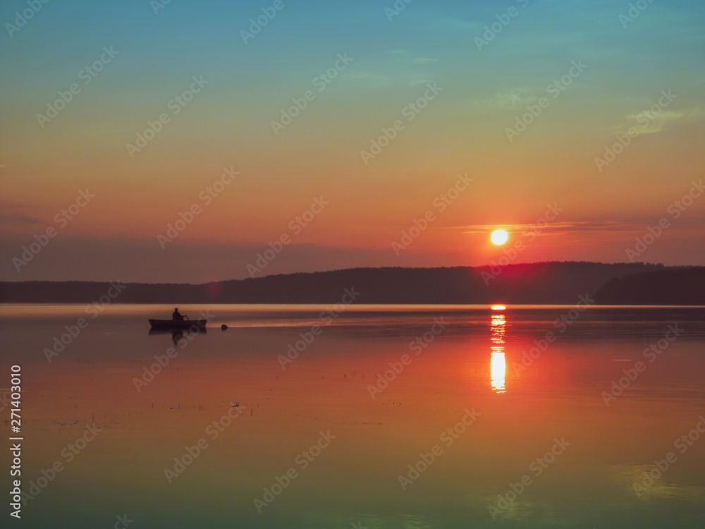 Fishing boat on lake. Idyllic early morning view of quiet water, sky and sun - sunset or sunrise. Summer landscape in the morning or evening.