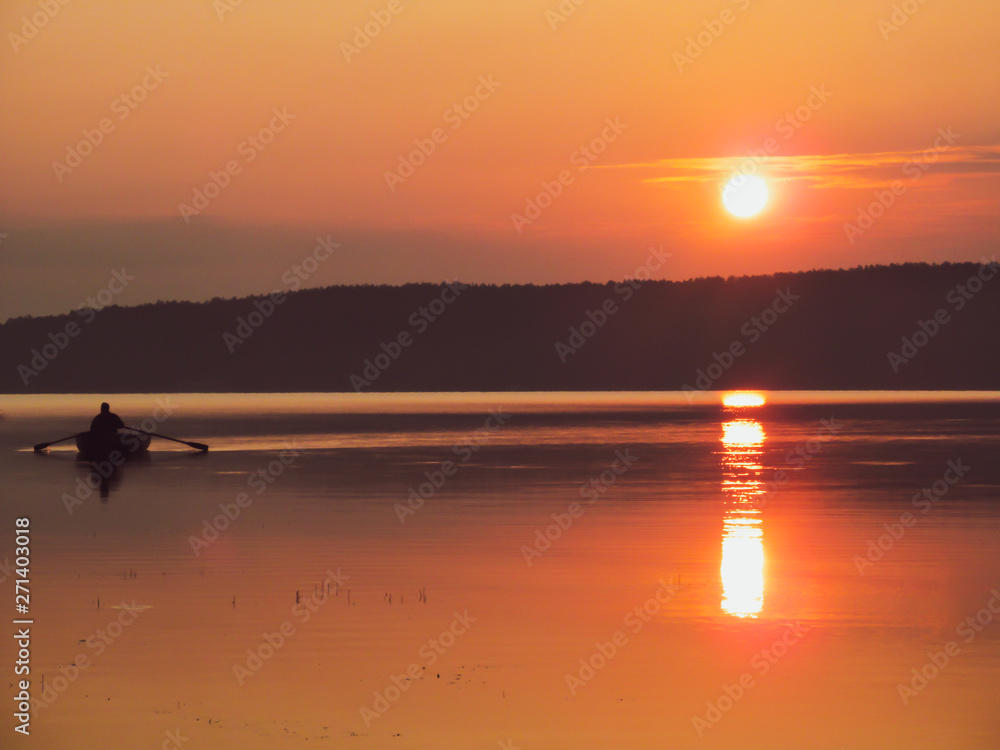 Fishing boat on lake. Idyllic early morning view of quiet water, sky and sun - sunset or sunrise. Summer landscape in the morning or evening.