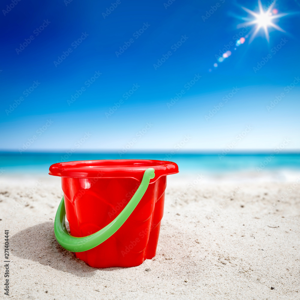 Red plastic bucket with free space for your product. The possibility of mounting bottles with drink, ice cream, food or other products. Blurry beach with people and ocean view. Red plastic bucket with free space for your product. The possibility of mounting bottles with drink, ice cream, food or other products. Blurry beach with people and ocean view.