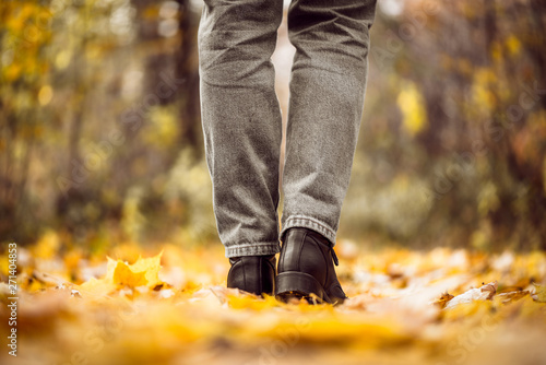 A girl in jeans and boots walks through the autumn forest or parkland. View of women s legs in the multi-colored foliage in the Indian summer season