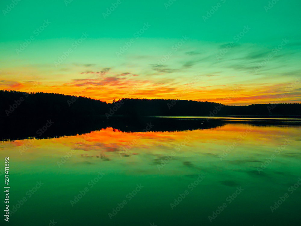 Bright colorful sunset over a lake. Beautiful reflection by a tranquil water of amazing sky and the lakeside at sundown in the summer evening. Lake Elovoe (Spruce Lake), South Ural, Russia.
