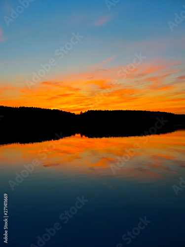 Bright colorful sunset over a lake. Beautiful reflection by a tranquil water of amazing sky and the lakeside at sundown in the summer evening. Lake Elovoe (Spruce Lake), South Ural, Russia.