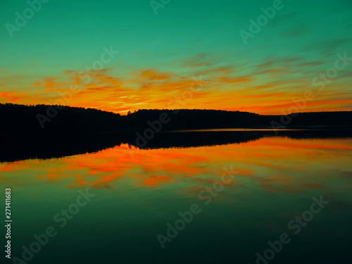 Bright colorful sunset over a lake. Beautiful reflection by a tranquil water of amazing sky and the lakeside at sundown in the summer evening. Lake Elovoe  Spruce Lake   South Ural  Russia.