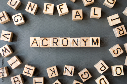 the word acronym wooden cubes with burnt letters, use of acronyms in the modern world, gray background top view, scattered cubes around random letters
