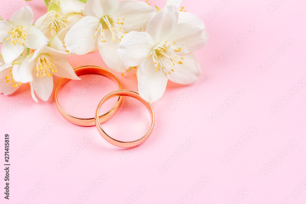pair of gold wedding rings and white Jasmine flowers on pink background with copy space pair of gold wedding rings and white Jasmine flowers on pink background with copy space