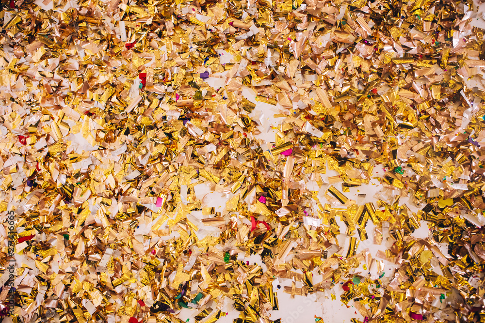 Golden Confetti on a wooden floor reflecting red stage spotlight causing colorful glow Golden Confetti on a wooden floor reflecting red stage spotlight causing colorful glow