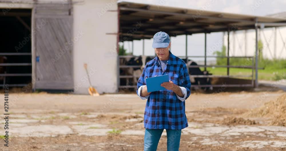 Farmer gesturing while writing on clipboard against barn Farmer gesturing while writing on clipboard against barn
