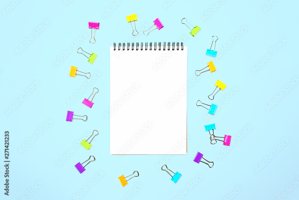 Back to school background with notepad, colorful paper clips on pastel blue backdrop. Flat lay, top view, copy space. Back to school background with notepad, colorful paper clips on pastel blue backdrop. Flat lay, top view, copy space.