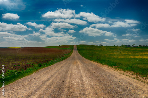 Gravel country road through farm fields and meadow