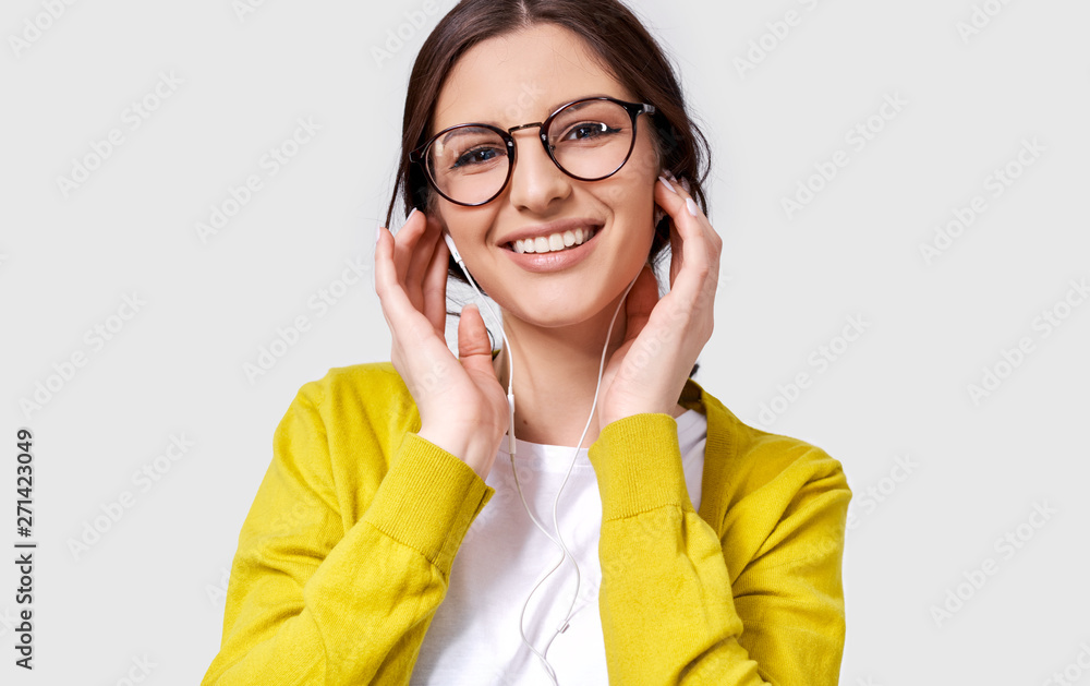 Closeup shot of pretty Caucasian young woman smiling broadly, listening the music on headphones. Happy female enjoying the favorite songs on earphones. People, music and technology concept Closeup shot of pretty Caucasian young woman smiling broadly, listening the music on headphones. Happy female enjoying the favorite songs on earphones. People, music and technology concept