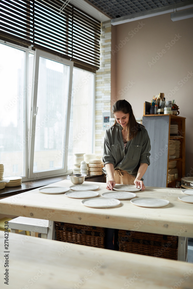 Portrait of modern female artisan arranging handmade ceramic plates in pottery workshop, copy space Portrait of modern female artisan arranging handmade ceramic plates in pottery workshop, copy space