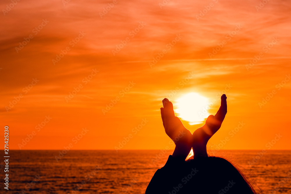 girl silhouette on sunset sea background. girl holds the sun in his hands.