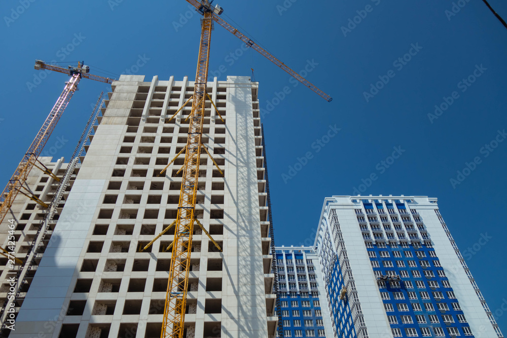 White high-rise building under construction and tower cranes against the blue sky. White high-rise building under construction and tower cranes against the blue sky.