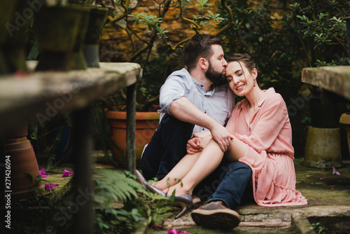 Young loving cheerful caucasian couple in glass greenhouse among colorful azalea flowers. Happy man and woman hugging and holding hands, spending time togehter. © anna_gorbenko