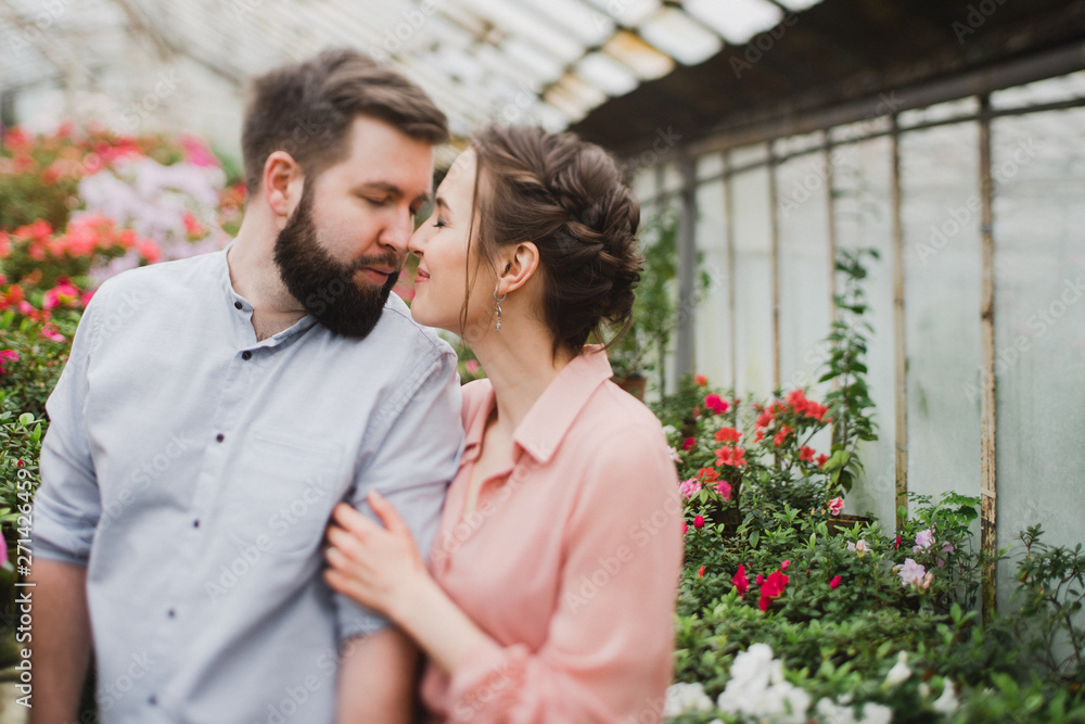 Young loving cheerful caucasian couple in glass greenhouse among colorful azalea flowers. Happy man and woman hugging and holding hands, spending time togehter. Young loving cheerful caucasian couple in glass greenhouse among colorful azalea flowers. Happy man and woman hugging and holding hands, spending time togehter.
