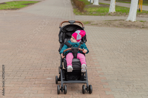 Little girl sitting in a baby carriage on the street