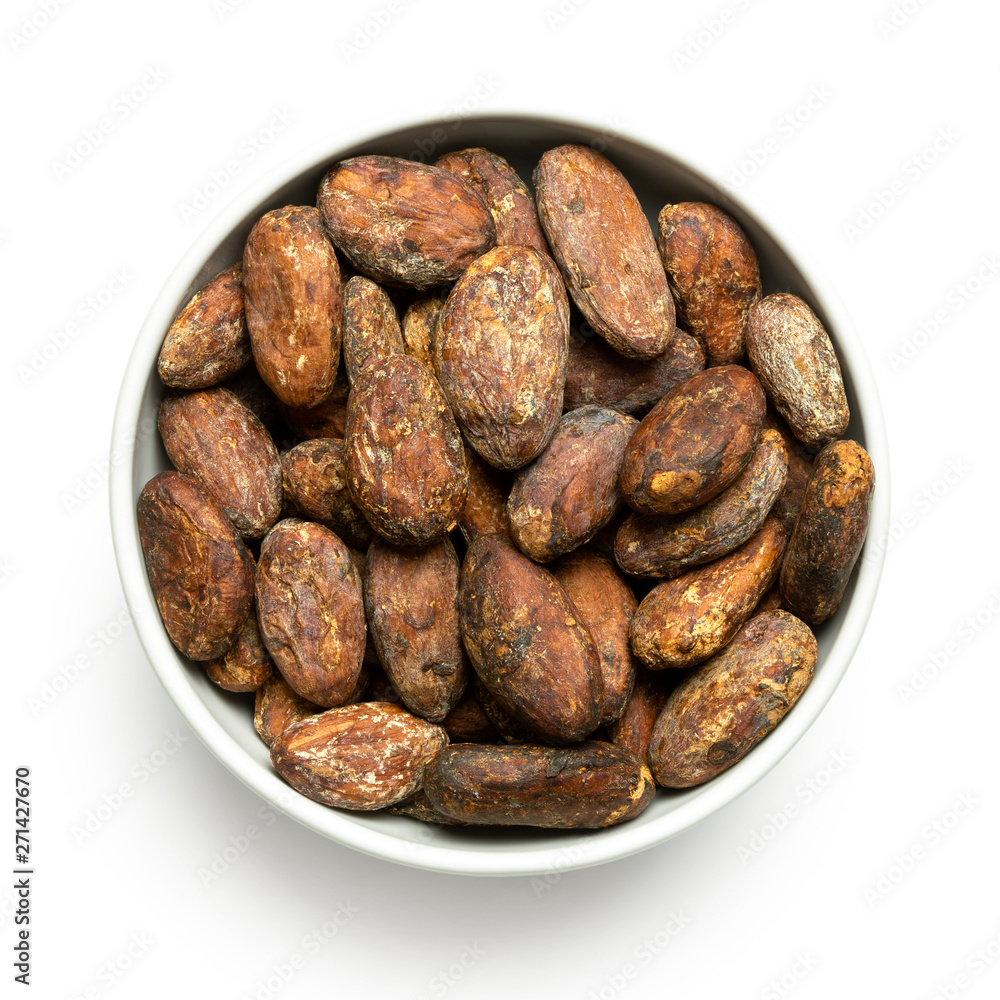 Roasted unpeeled cocoa beans in a white ceramic bowl isolated on white from above.