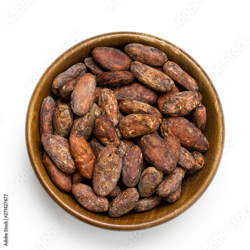 Roasted unpeeled cocoa beans in a brown wooden bowl isolated on white from above.