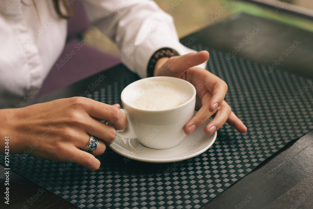 Woman with beautiful hands is drinking coffee in cafe. Close-up cappuccino in white cup, image with film effect and author processing. Woman with beautiful hands is drinking coffee in cafe. Close-up cappuccino in white cup, image with film effect and author processing.