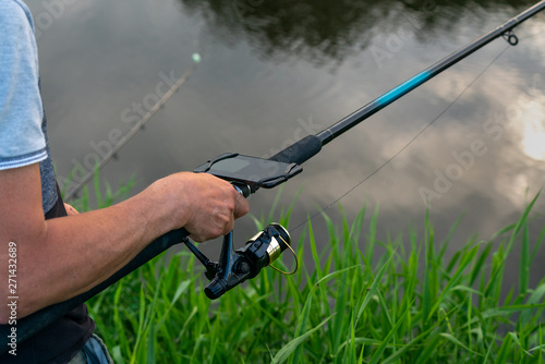 Close-up on the hand of an anglerfish measuring the depth of water in the river. On the display of the smartphone attached to the fishing rod, it reads the measurement results.