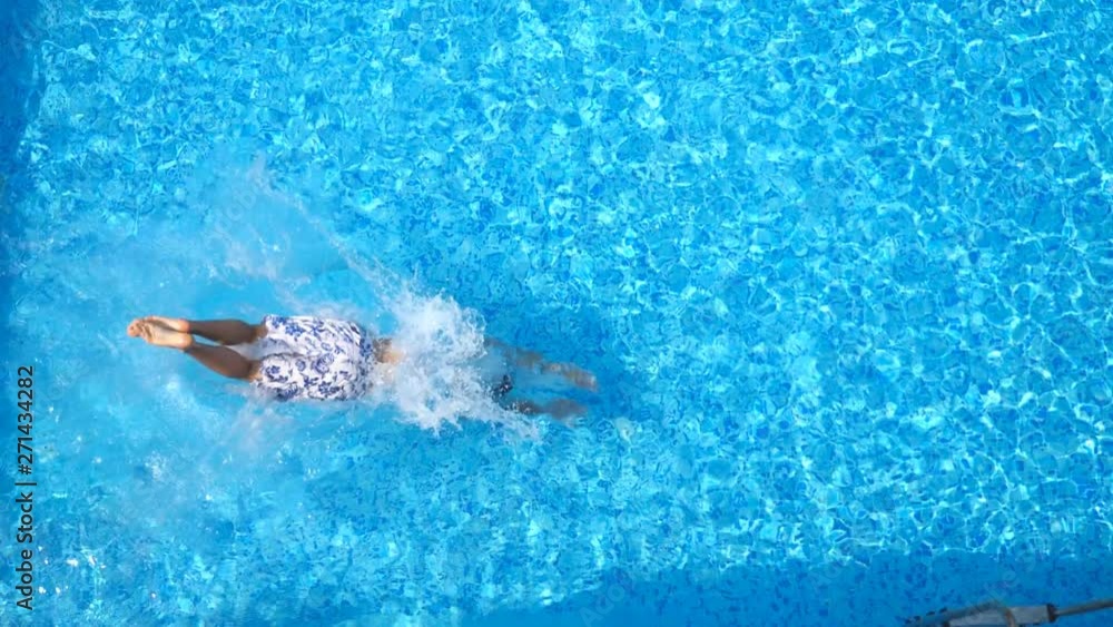 Top view of young man jumping in pool and splashing crystal clear water. Unrecognizable guy swimming under water in basin at sunny day. Boy relaxing during summer vacation. Slow motion Close up