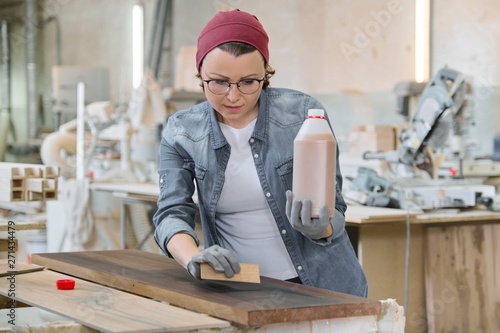 Mature craftswoman working in woodshop. Female painting wooden board with oil, varnish.