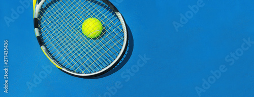 Summer sport concept with tennis ball and racket on blue hard tennis court. Flat lay, top view, copy space. Blue and yellow, banner size.