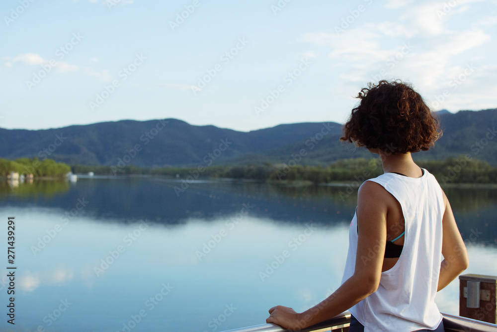 SUMMER WOMAN BACKWARDS WATCHING NATURE AT LAKE LANDSCAPE.