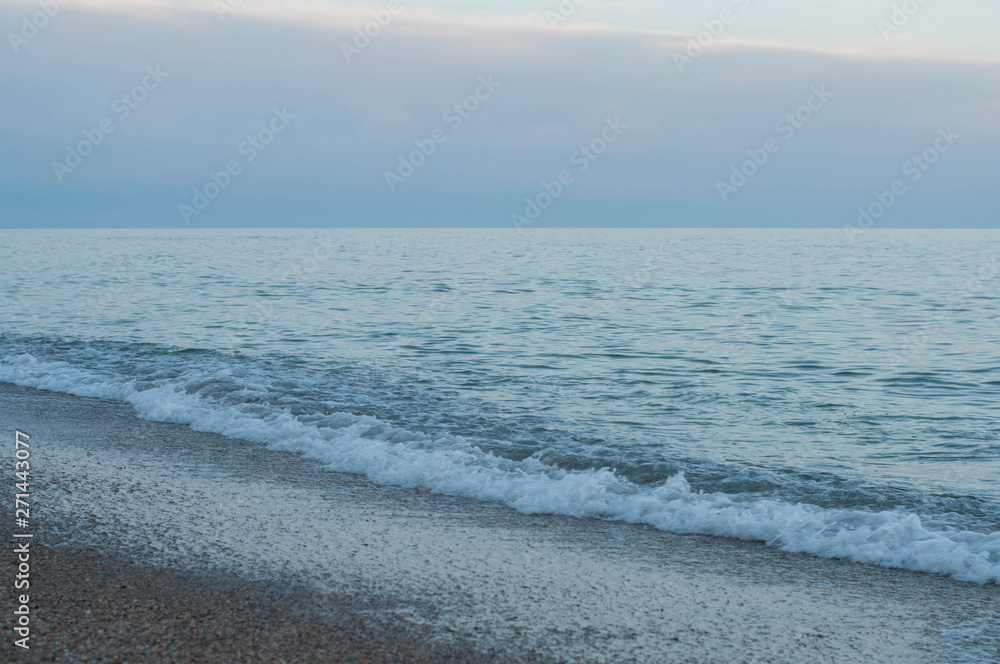 Sunset calm sea surf in violet dusk evening with blue smoky sky. Seascape of Black sea coast. Waving sea tides come to wet beach sand. Diagonal coastline. Travel scenery. Tranquil landscape at seaside