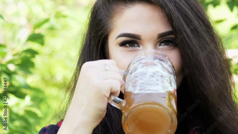 Portrait of young happy beautiful woman which drinks beer from glass, quenches thirst, smile and looking at camera in a sunny park Portrait of young happy beautiful woman which drinks beer from glass, quenches thirst, smile and looking at camera in a sunny park