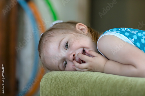 Little cheerful girl is lying on the sofa in the room. Emotional portrait.