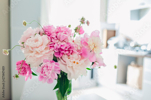 Pink peonies. Modern kitchen design. Interior of white and silver kitchen decorated with flowers.