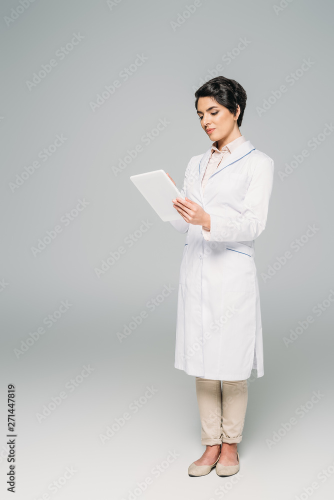 beautiful mixed race doctor in white coat using digital tablet on grey background beautiful mixed race doctor in white coat using digital tablet on grey background