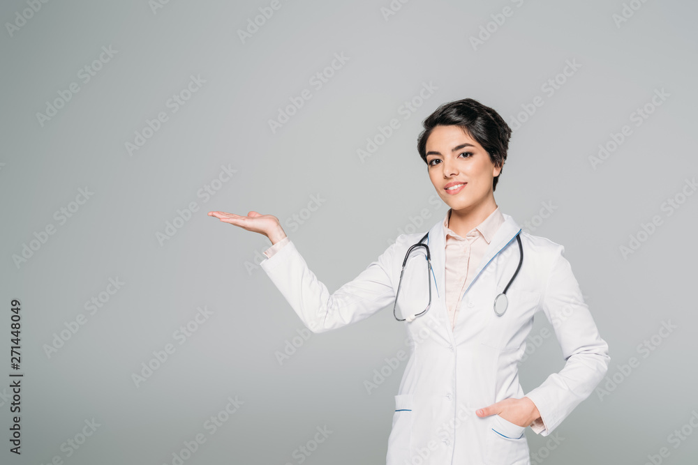pretty mixed race doctor pointing with hand while looking at camera isolated on grey pretty mixed race doctor pointing with hand while looking at camera isolated on grey