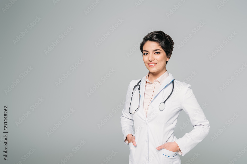 cheerful mixed race doctor with stethoscope posing at camera with hands in pockets isolated on grey cheerful mixed race doctor with stethoscope posing at camera with hands in pockets isolated on grey