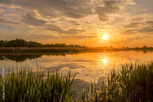 Fototapeta Naklejka Na Ścianę i Meble -  Sunset above the pond or lake with cloudy sky at summer and water reflection.