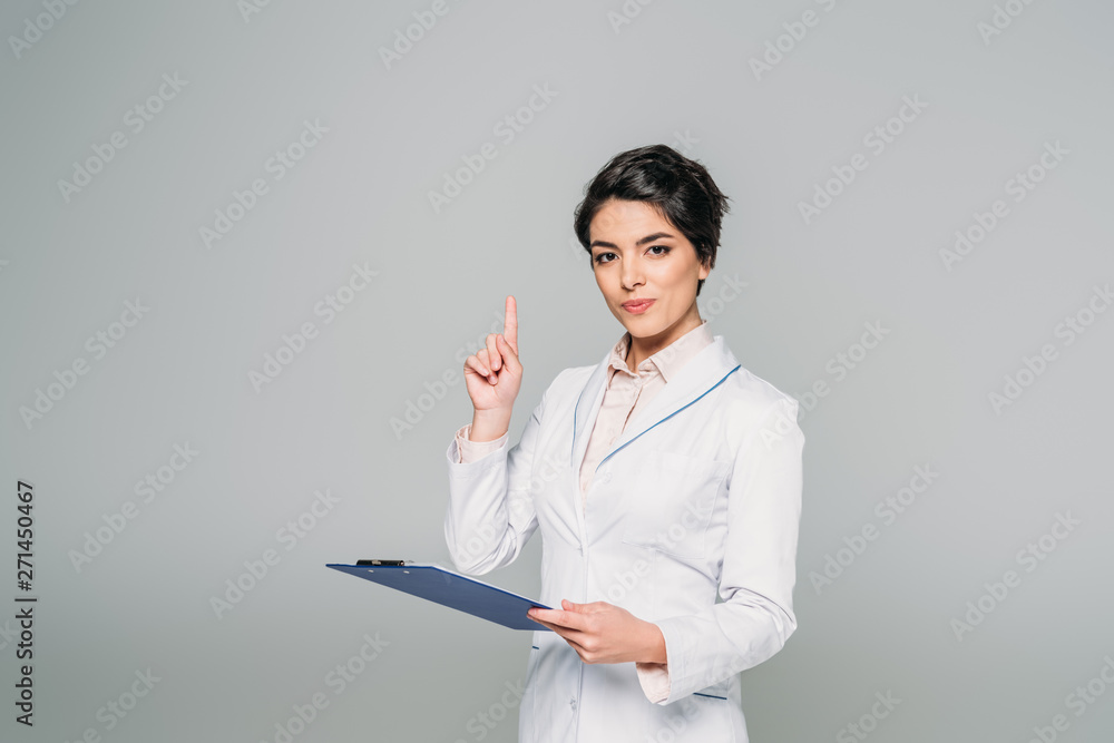 pretty mixed race doctor showing idea sign while holding clipboard isolated on grey pretty mixed race doctor showing idea sign while holding clipboard isolated on grey