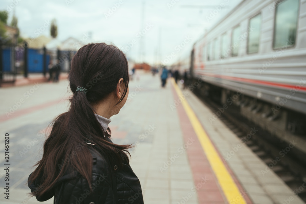 Fototapeta premium Young woman waiting for arrival of train. Side view unrecognizable young brunette female standing on platform and waiting for arrival of train
