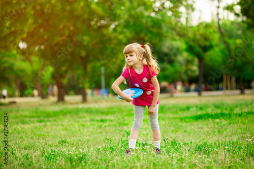Child girl playing with a frisbee in summer park