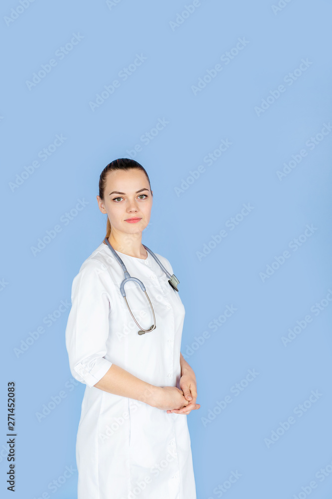 Young female doctor in white uniform with phonendoscope on her neck on blue background with space for text. Healthcare concept Young female doctor in white uniform with phonendoscope on her neck on blue background with space for text. Healthcare concept
