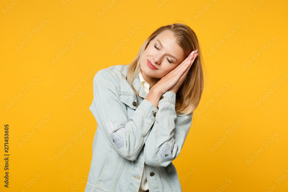 Portrait of relaxed pretty young woman in denim casual clothes sleep with folded hands under cheek isolated on yellow orange wall background in studio. People lifestyle concept. Mock up copy space. Portrait of relaxed pretty young woman in denim casual clothes sleep with folded hands under cheek isolated on yellow orange wall background in studio. People lifestyle concept. Mock up copy space.