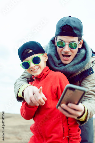 young father with his son having fun outside in spring field, happy family smiling, lifestyle people making selfie wearing sunglasses