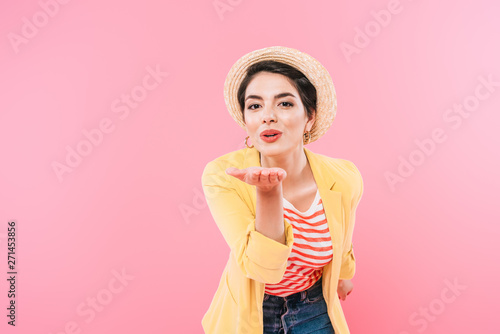 cheerful mixed race woman sending air kiss at camera isolated on pink