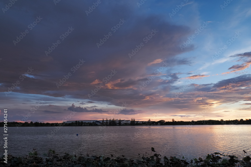 Lake view evening of dark clouds moving above reservoir with yellow sun light and cloudy sky background, sunset at Krajub Reservoir, attraction in Ban Pong, Ratchaburi, Thailand.