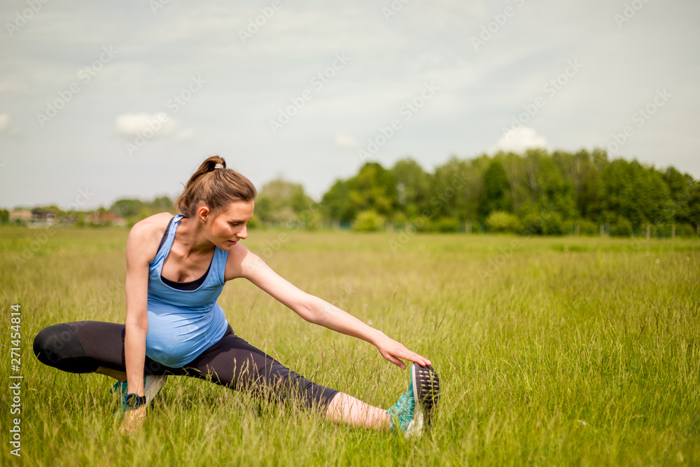 Pregnant woman fitness exercises on grass at sunny day