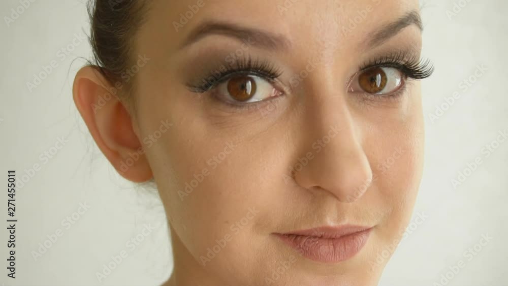 Female face with long false eyelashes and brown eyes looks at camera. Closeup beautiful girl model with handsome makeup on white background Female face with long false eyelashes and brown eyes looks at camera. Closeup beautiful girl model with handsome makeup on white background