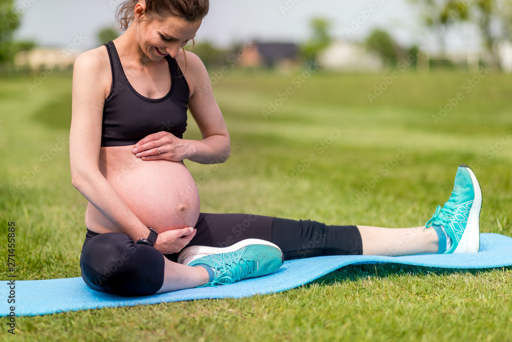 Pregnant woman fitness exercises on grass at sunny day