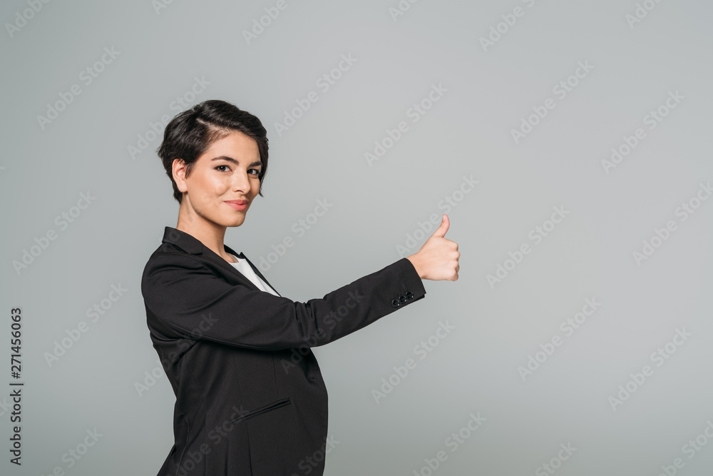 smiling mixed race businesswoman showing thumb up and looking at camera isolated on grey smiling mixed race businesswoman showing thumb up and looking at camera isolated on grey