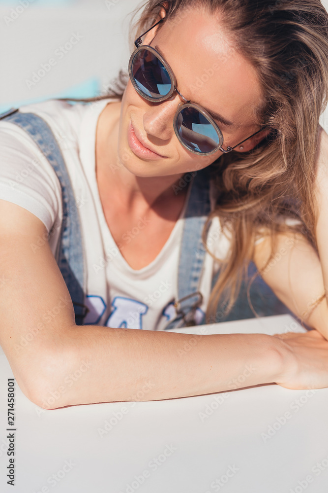 Naklejka premium Successful young woman in sunglasses happily resting and sunbathing in the sun near the sea while relaxing on a sunny hot summer day. Long-awaited vacation concept