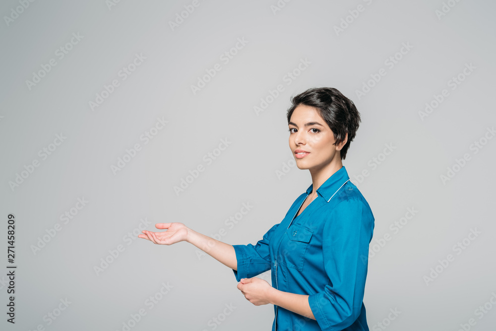 beautiful mixed race doctor gesturing while looking at camera isolated on grey beautiful mixed race doctor gesturing while looking at camera isolated on grey